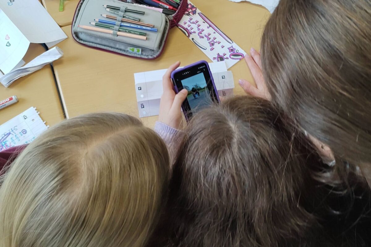 Drei Schülerinnen erarbeiten einen TikTok-Beitrag am Smartphone